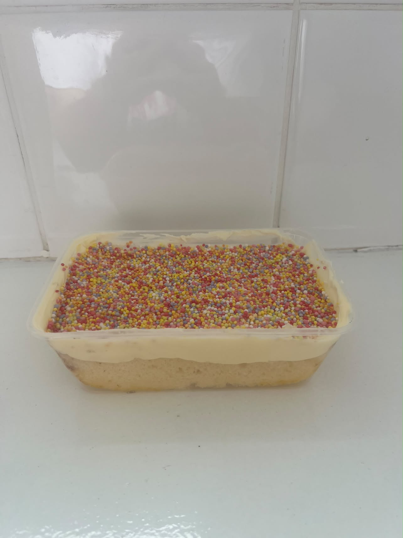 Dot Cake tub by Bella & Bloom Co. topped with vanilla icing and rainbow hundreds and thousands